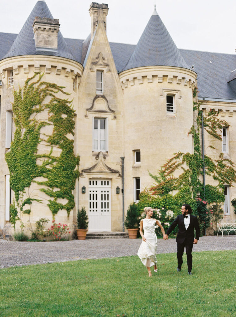 Tristan & Meredith walking hand-in-hand on the grass in front of a historic chateau