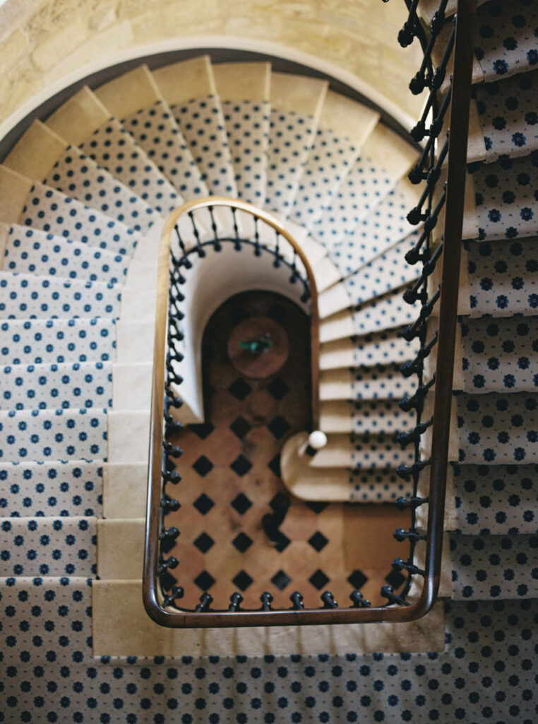 Spiral staircase with patterned tiles leads down to a lower level, viewed from above