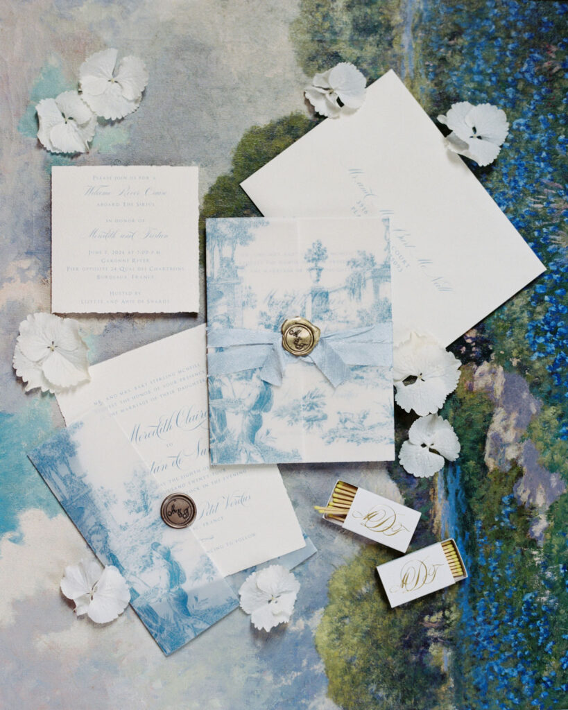 Flat lay of wedding stationery featuring invitations, RSVP cards, and envelopes with blue floral patterns and calligraphy