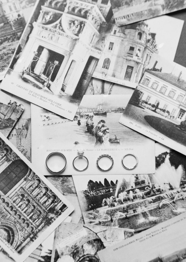 Vntage black-and-white postcards featuring various historic buildings and landmarks is spread out with five rings positioned in a line on top of one of the postcards