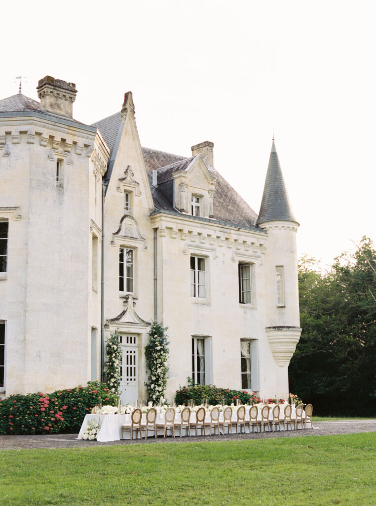 Luxurious long dining table decorated with white flowers set up outside Château Le Petit Verdus