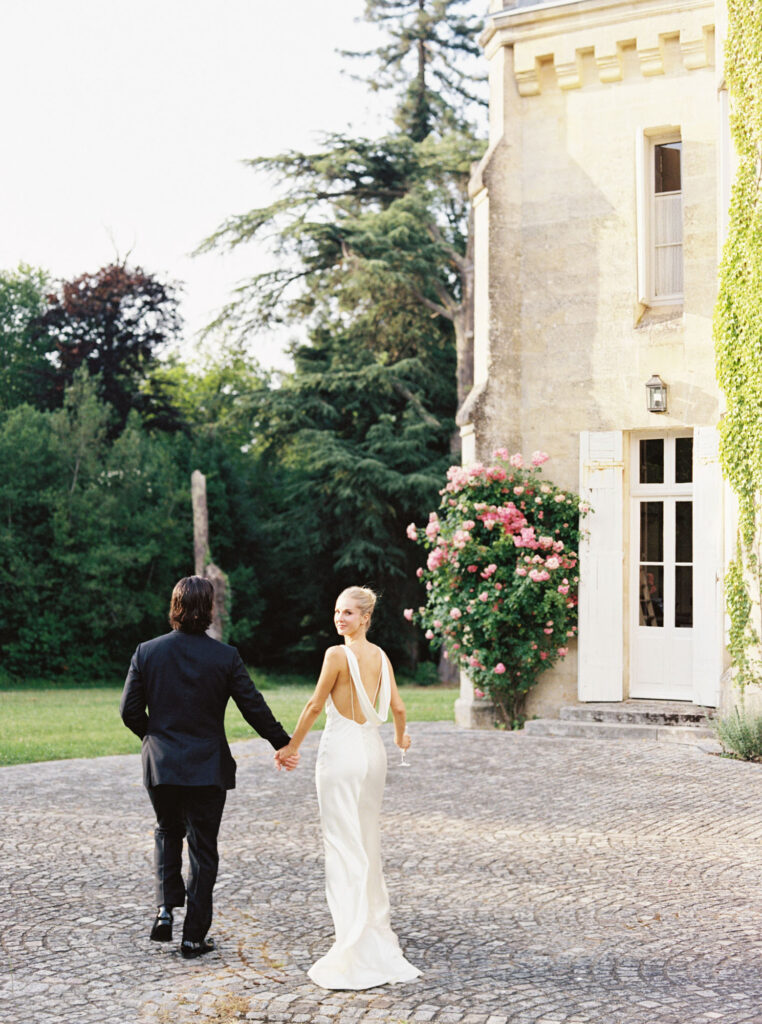 Meredith and Tristan holds hands and walks away from the camera on a cobblestone path