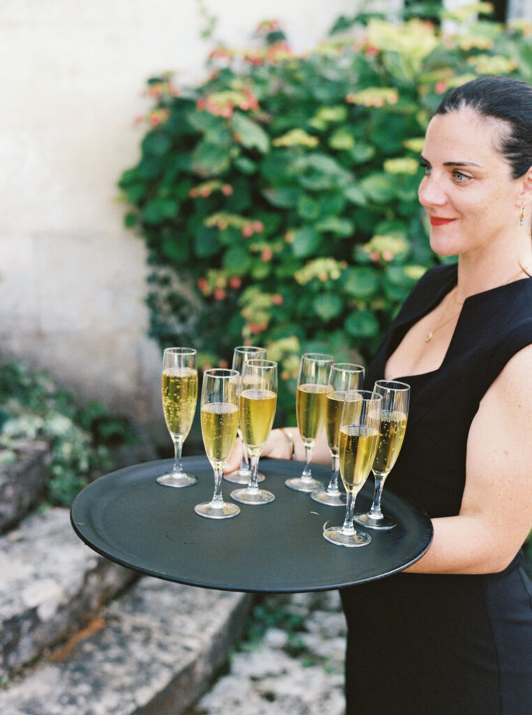 Woman holding a round black tray with eight champagne glasses filled with champagne