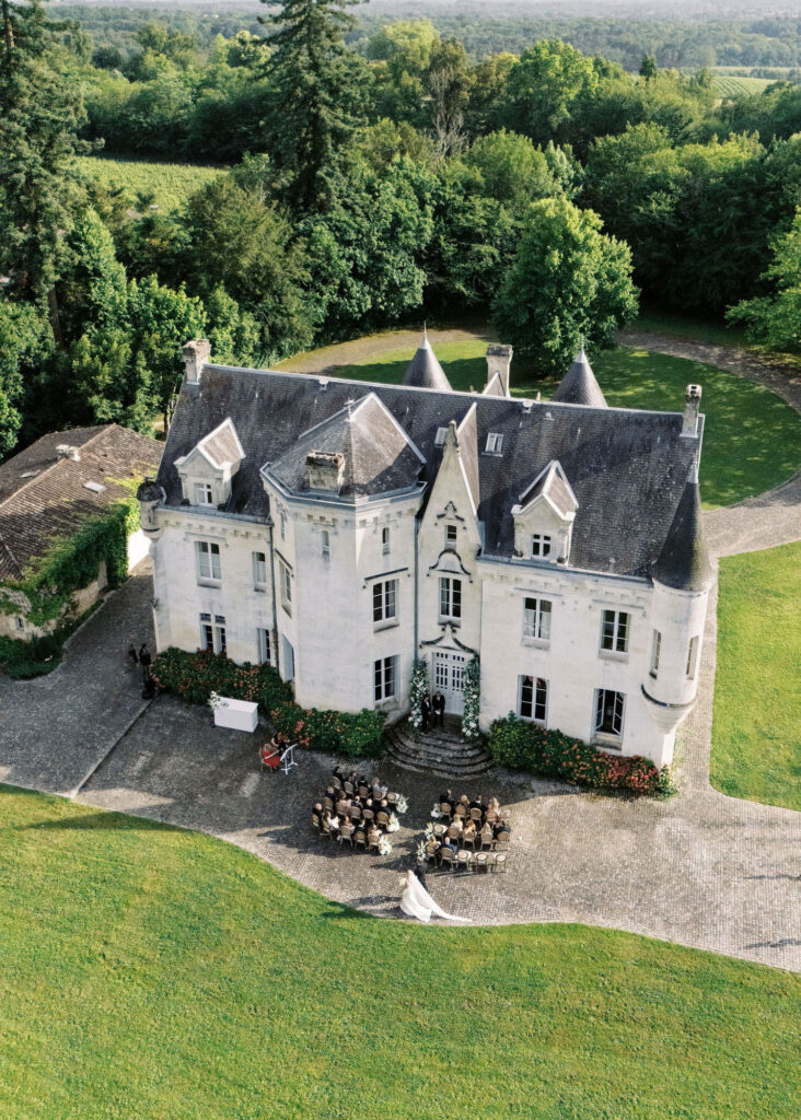 Aerial view of a wedding ceremony taking place in front of Château Le Petit Verdus surrounded by lush greenery and trees