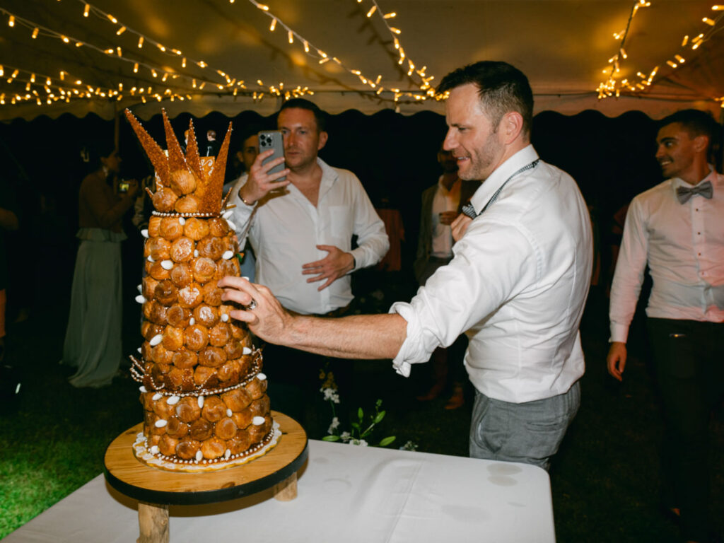 Person admires and touches the wedding cake while a guest captures the moment with his phone