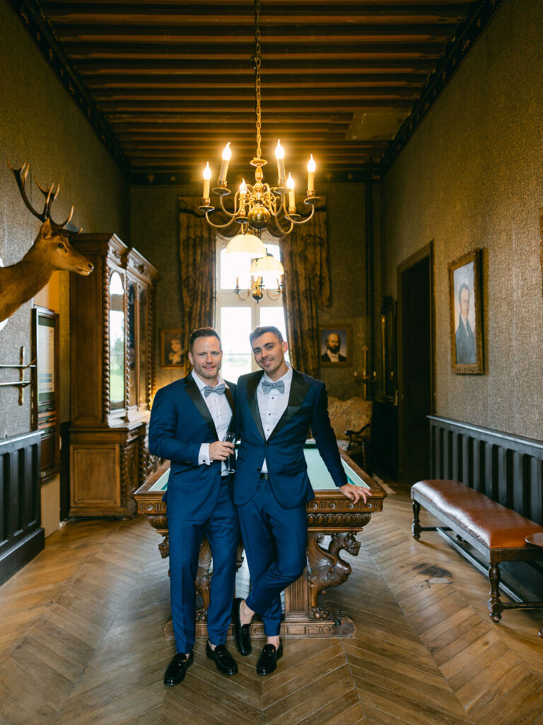 Kevin and Steven in blue suits standing together in a luxurious room with wooden accents and chandeliers preparing for their wedding