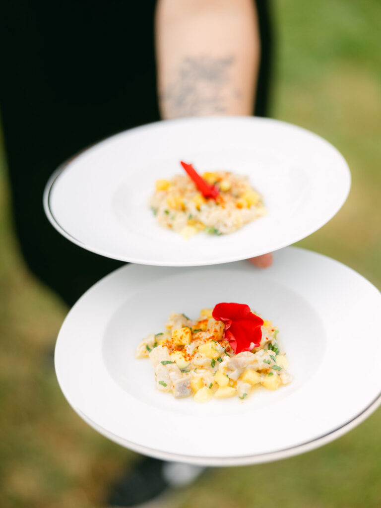 Two elegant plates of a colorful seafood dish with flower garnishes being served at the wedding