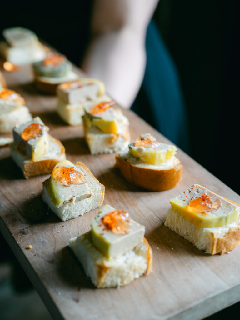 Bite-sized hors d'oeuvres featuring pâté on toast, displayed on a wooden board