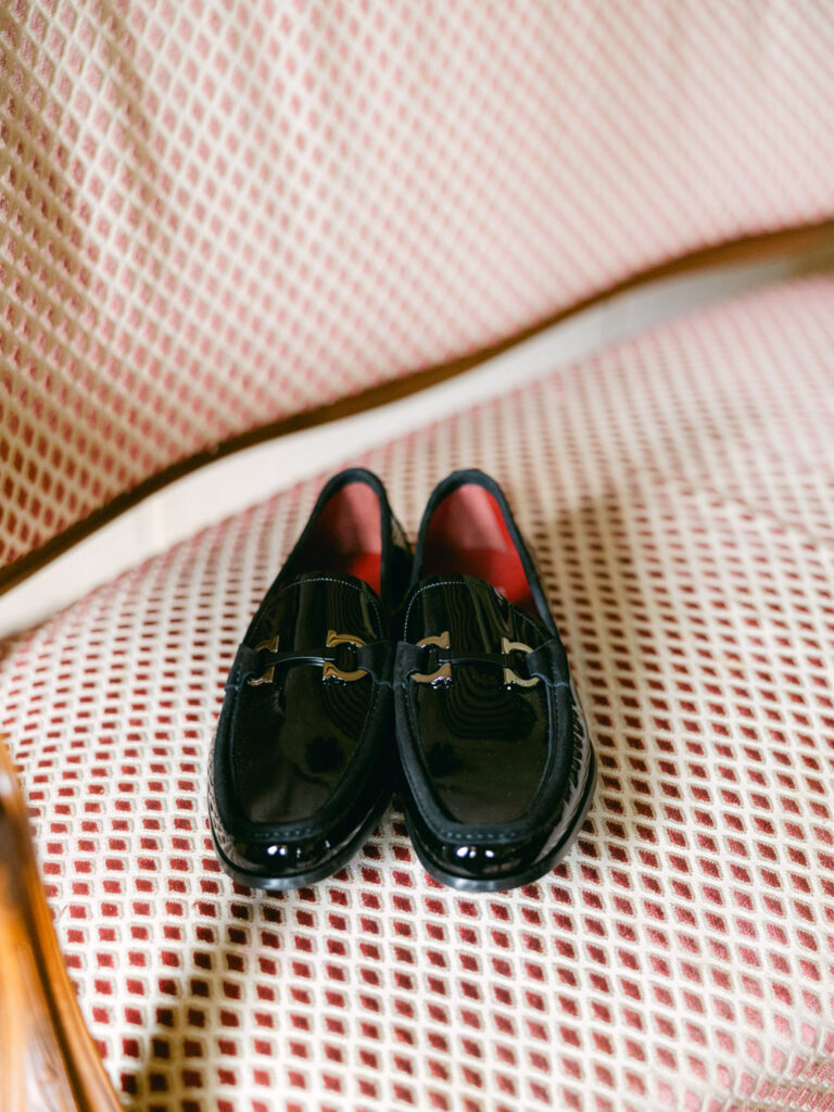 Pair of black loafers with metallic accents placed on a cushioned chair with a red and white patterned fabric