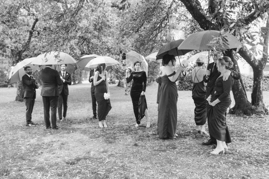 Wedding party with umbrellas standing outdoors on a rainy day