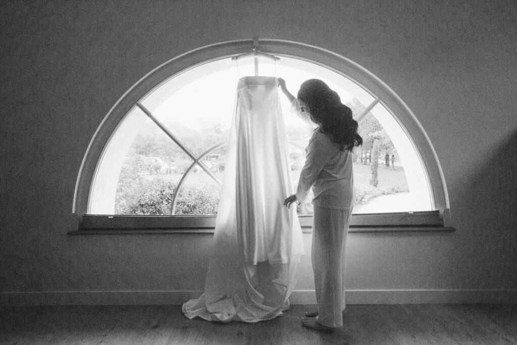 Bride admiring her wedding gown in front of a large arched window