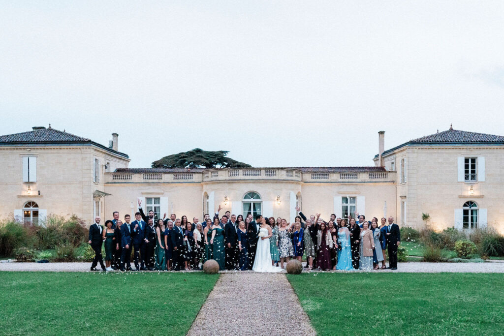 Bride and groom posing with wedding guests in front of a grand venue