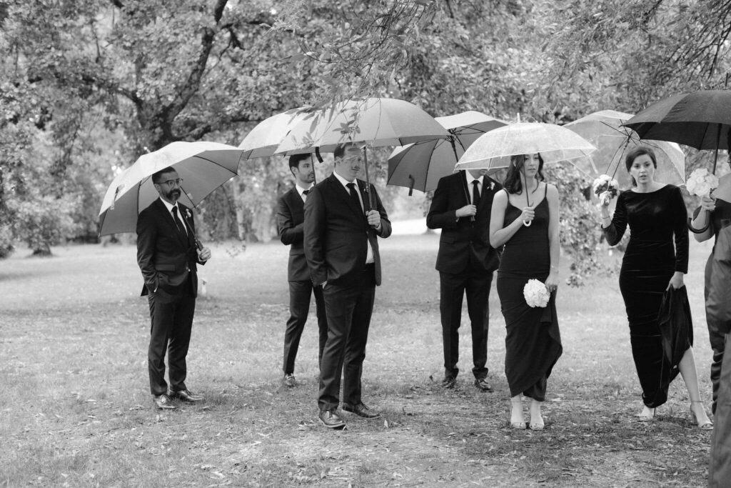 Black-and-white group photo with umbrellas on a rainy wedding day