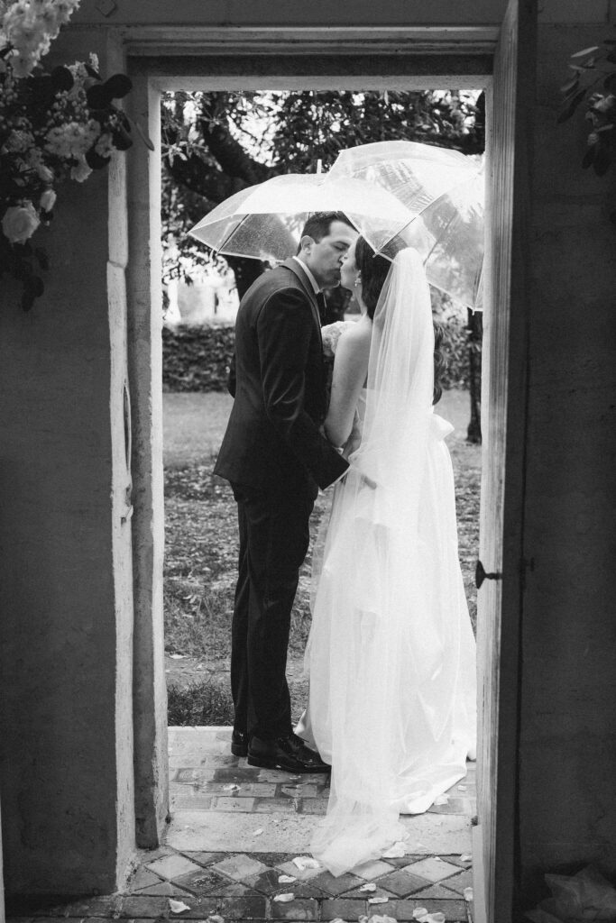 Bride and groom kissing under an umbrella on their rainy wedding day