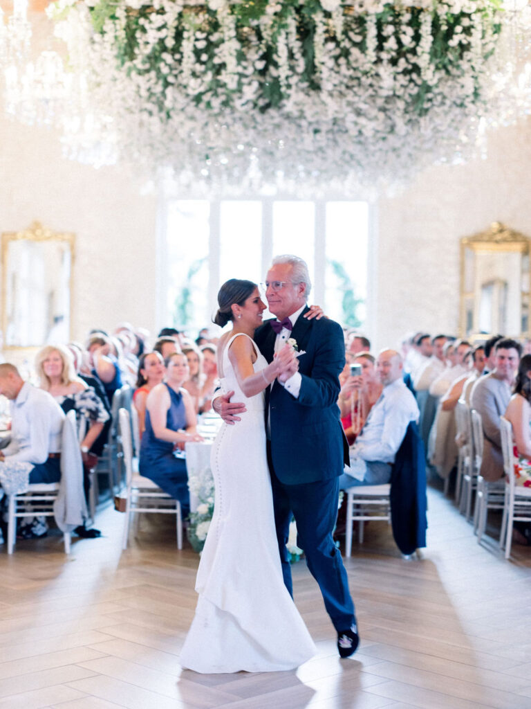 Bride dancing with her father under cascading floral chandeliers