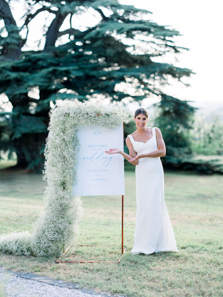 Alexandra pointing to the elegant welcome sign adorned with baby’s breath flowers