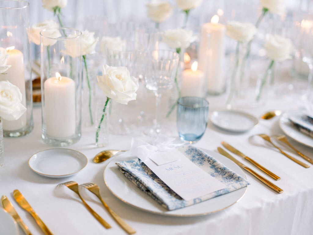 Close-up of the reception table setting with white roses, candles, and gold accents