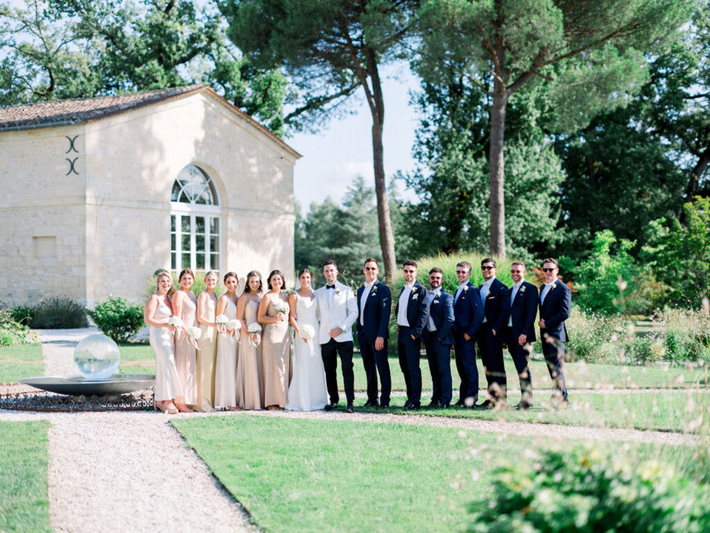 Wedding party posing outside Château Gassies with bridesmaids in champagne gowns and groomsmen in navy suits