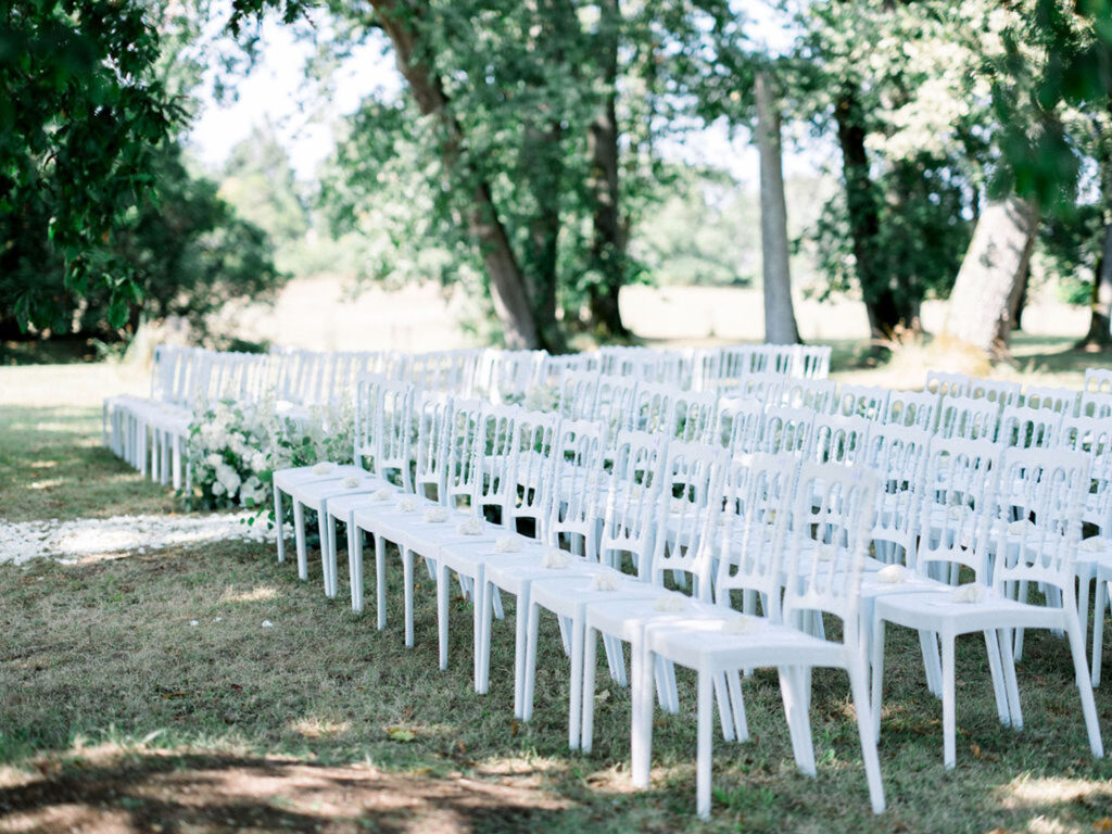 Rows of white chairs set up for an outdoor wedding ceremony