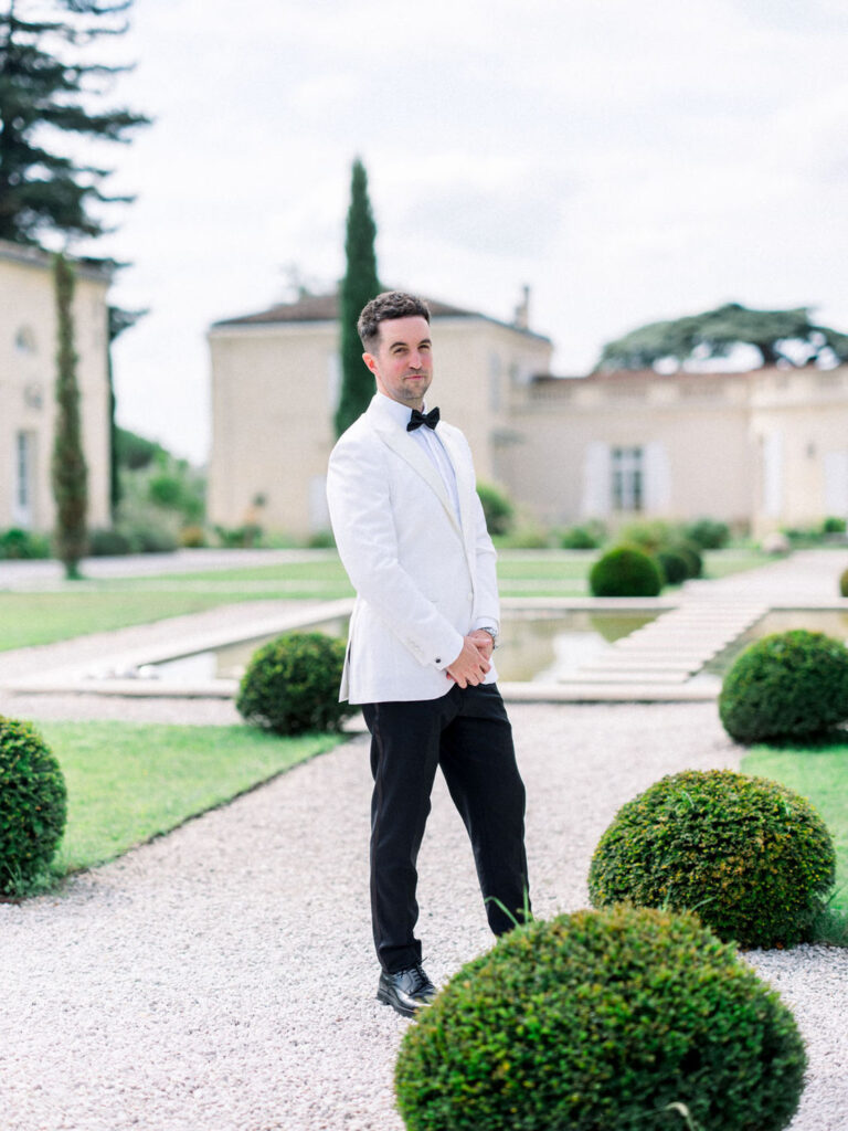 Thomas, the Groom posing confidently in a white tuxedo outside Château Gassies