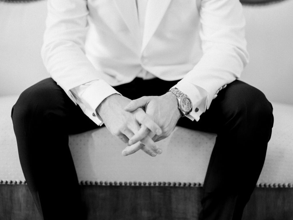 Groom’s hands resting on his lap, showcasing a watch and cufflinks