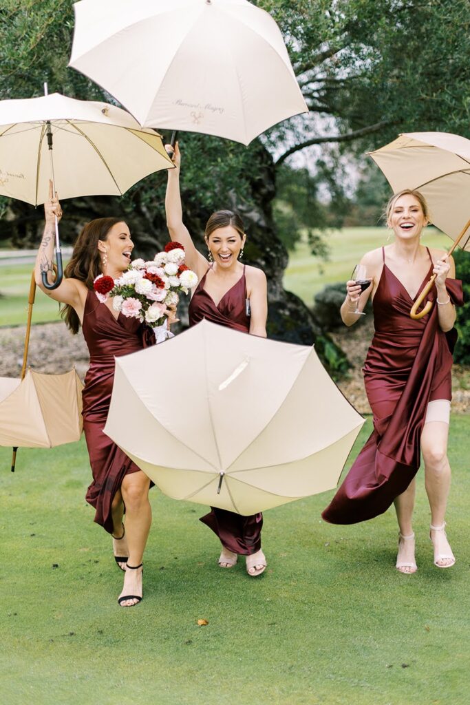 Bridesmaids laughing and running under umbrellas on a rainy wedding day