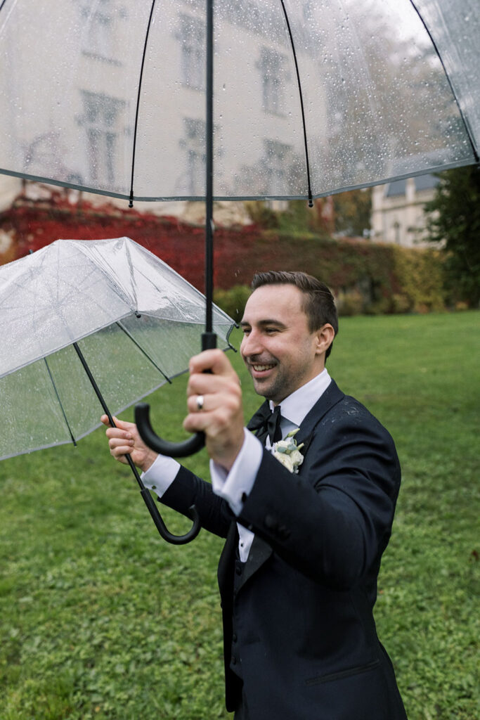 Groom happily holding two clear umbrellas