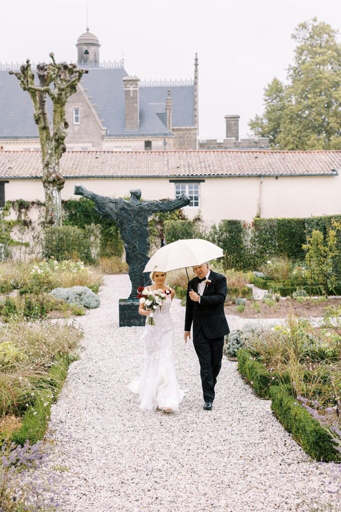 Bride and father using umbrellas during her wedding