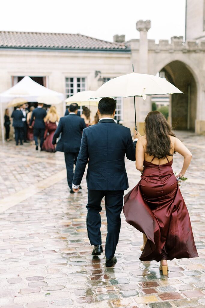 Wedding party under umbrellas strolling past the building