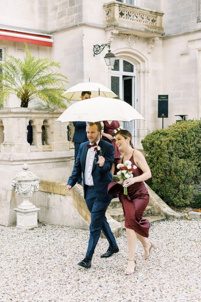 Wedding party descending steps under umbrellas at a chateau on a rainy day