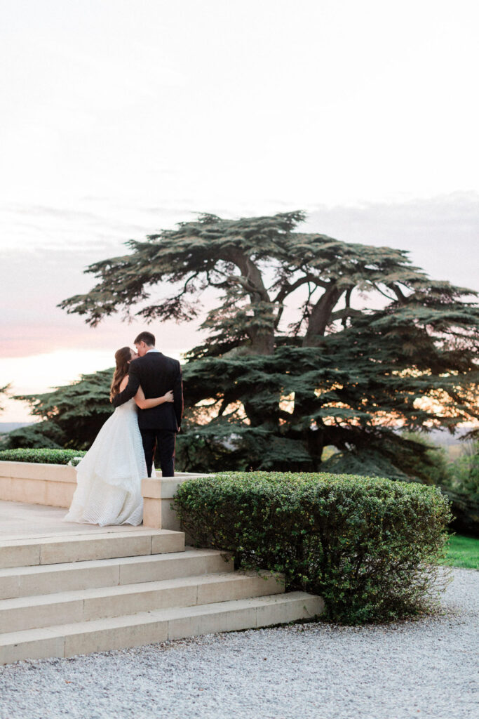 Lauren and Richie share an intimate moment on the chateau steps as the sun sets over their wedding party in Bordeaux