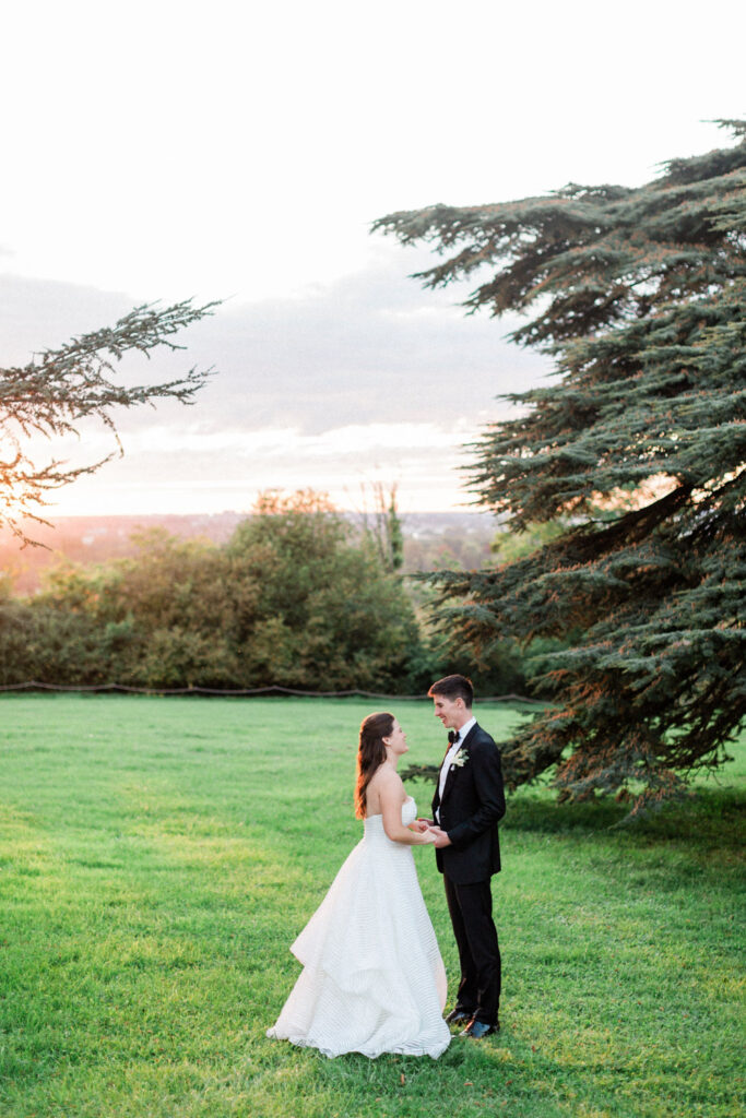 The newlyweds stand in a lush green field, framed by a dreamy Bordeaux sunset