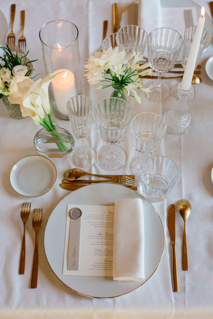 A sophisticated wedding tablescape featuring gold cutlery, crystal glassware, and soft candlelight