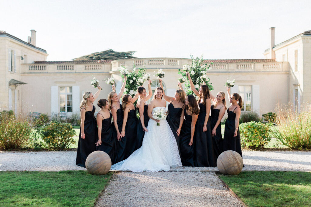 The bride and her bridesmaids joyfully celebrate in front of the château, tossing their bouquets in the air