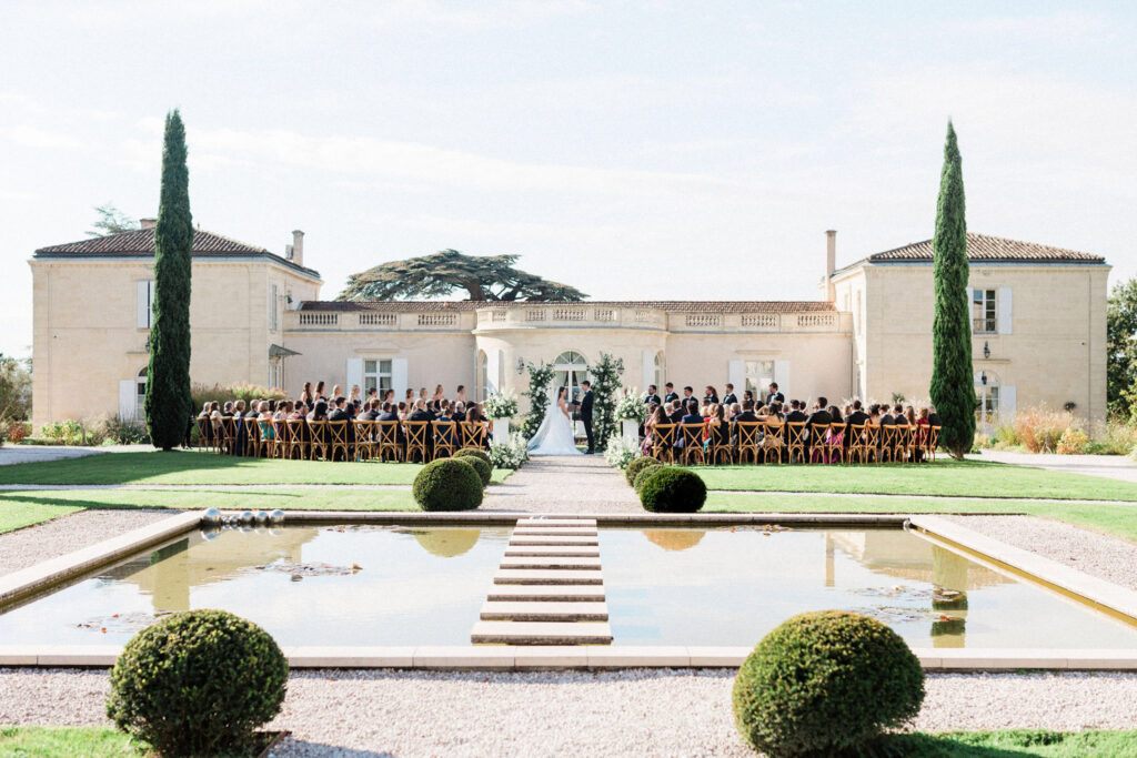 A stunning outdoor ceremony setup with a château backdrop, reflecting in the peaceful water feature