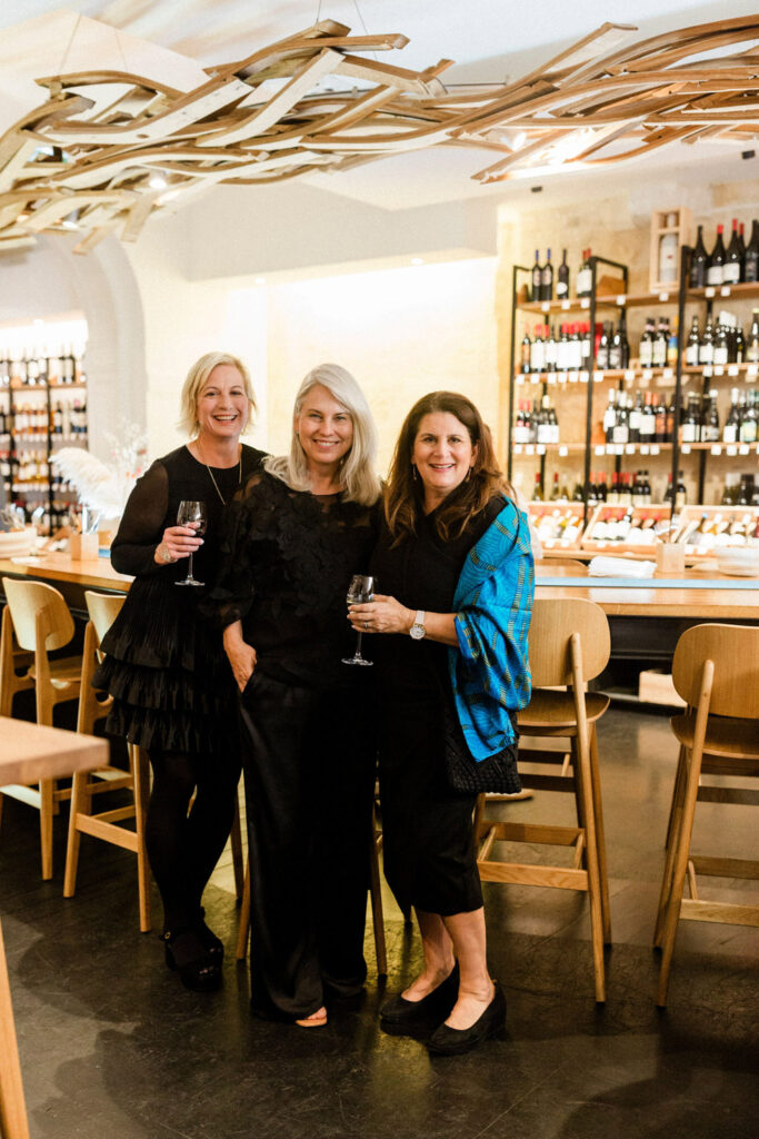 Three elegantly dressed women toasting with wine at a sophisticated wedding party in Bordeaux