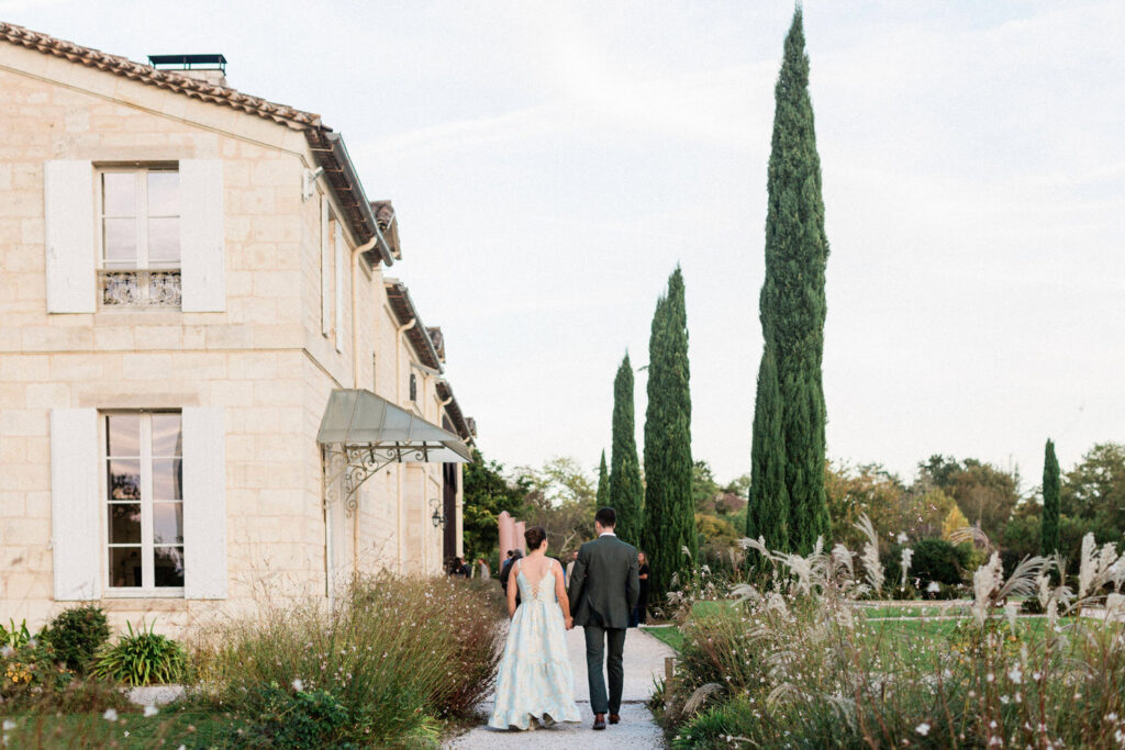 The bride and groom walking hand-in-hand through the lush gardens of their wedding venue for their welcome party