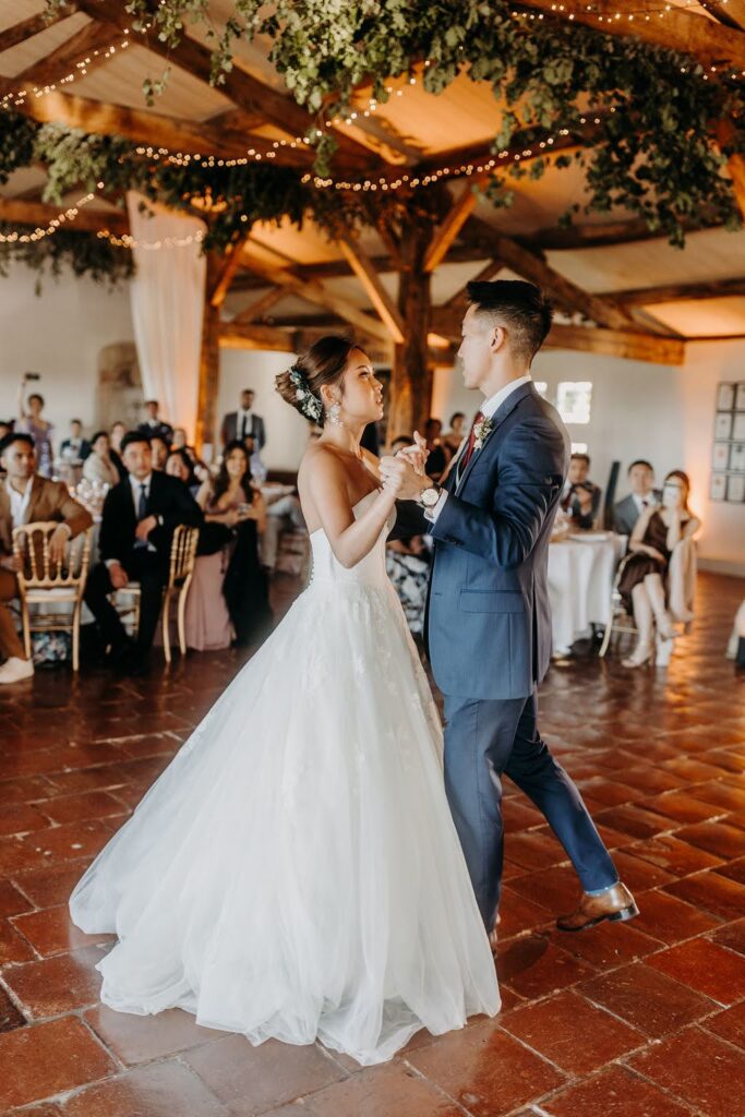 Couple’s first dance under rustic wooden beams.