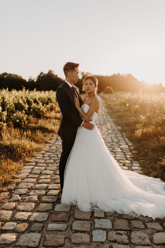 Sunset portrait of newlyweds on cobblestone path surrounded by Bordeaux vineyards.