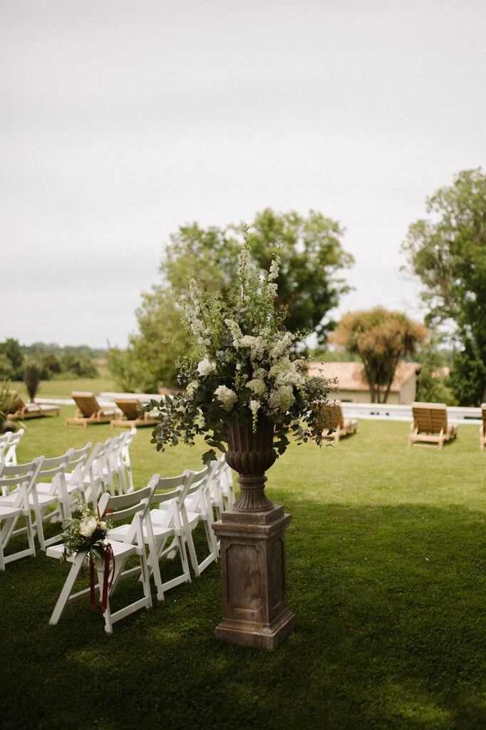 Outdoor ceremony setup with floral urn and white chairs.