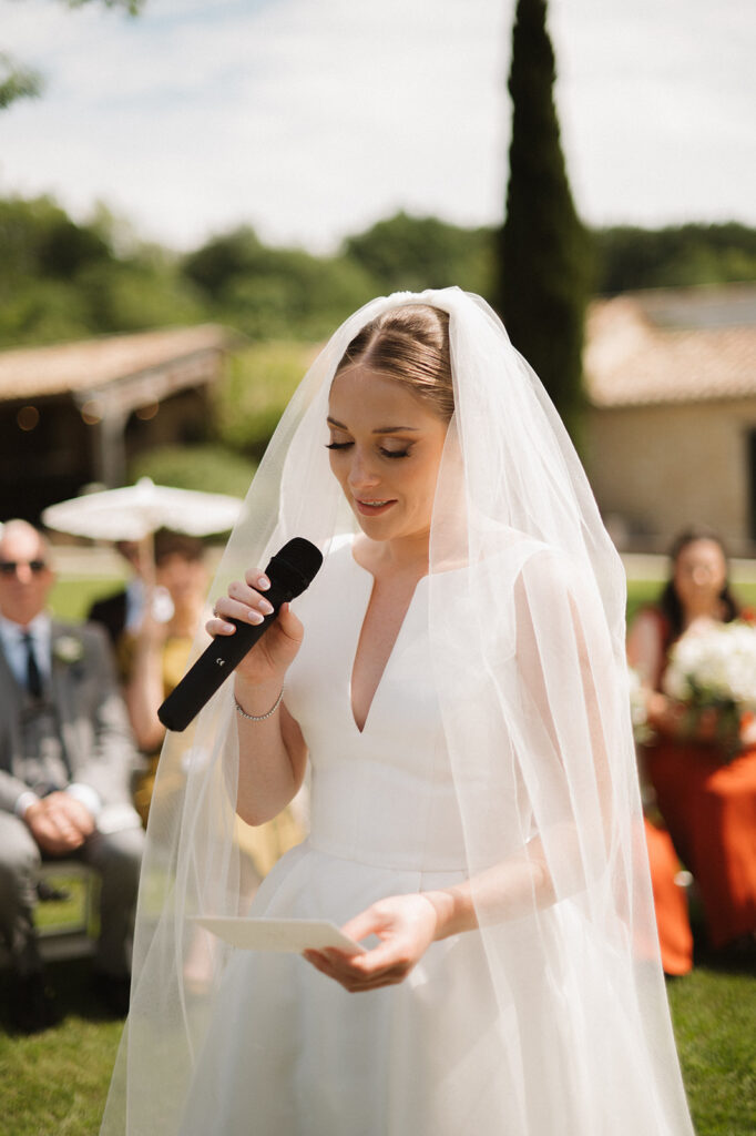 A bride reads her vows outdoors with a soft smile and heartfelt tone.