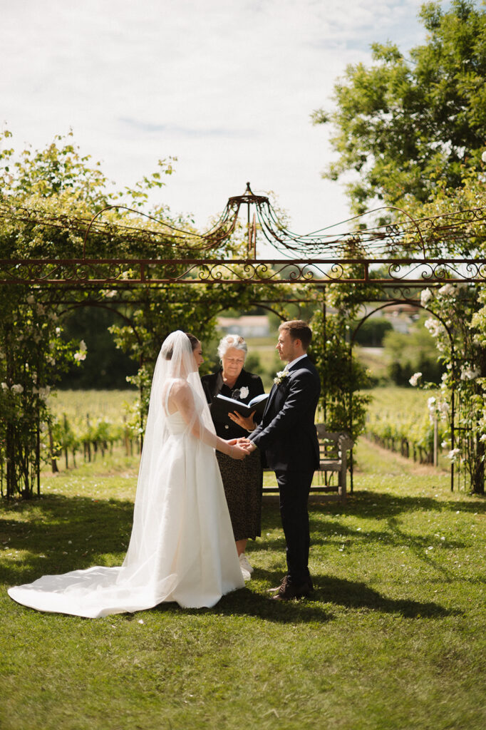 Bride and groom hold hands during an outdoor vineyard ceremony.