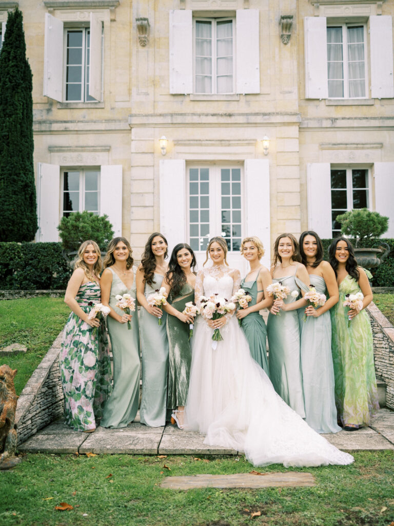 Bride and bridesmaids in green and floral dresses in front of a French château, illustrating bridal party.