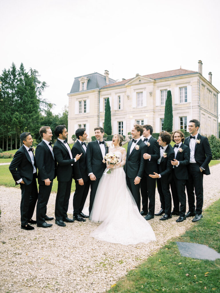 Groom and groomsmen laughing with the bride in front of a French château.