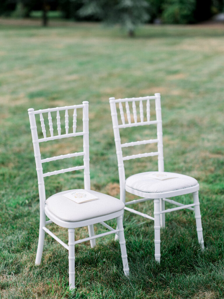 Two white chairs sit quietly with programs resting on their cushions.