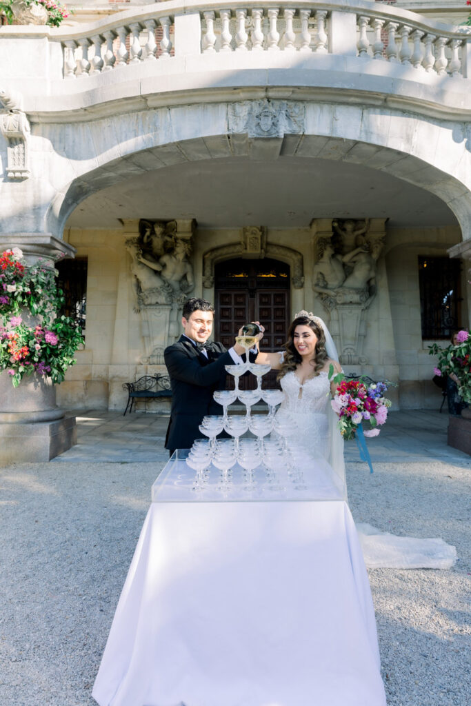 Couple pouring champagne into a tower of coupe glasses.