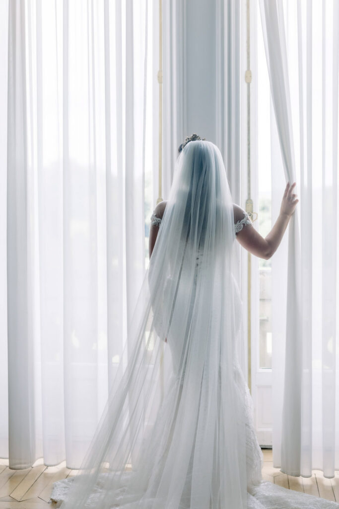 bride looking out sheer curtains in château bridal suite