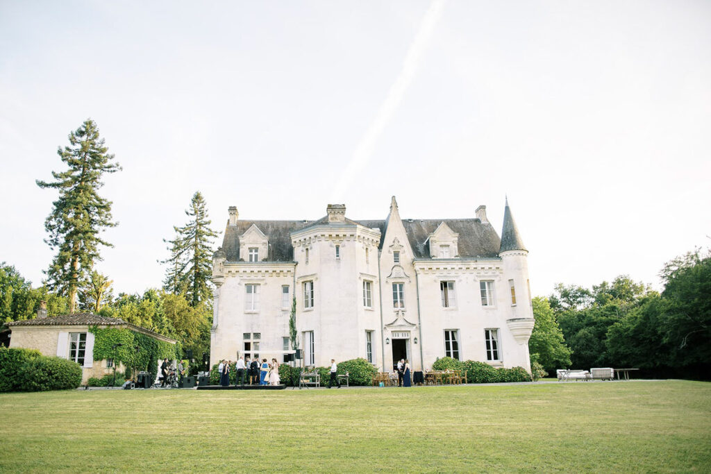 Guests gather on the lawn of a French chateau for a picturesque wedding reception.