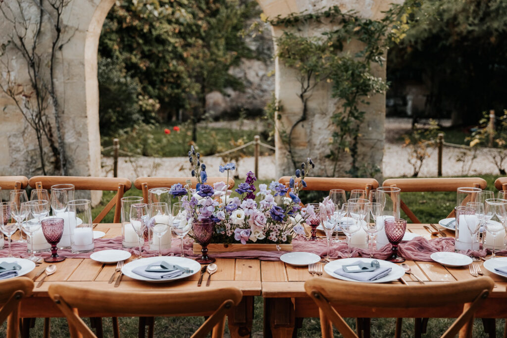 Long wooden dinner table set with lavender flowers, candles, and vintage glassware for a purple wedding inspiration