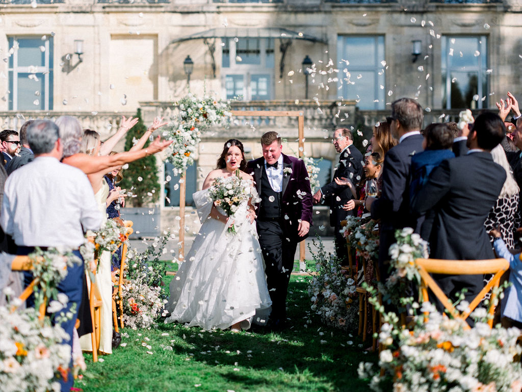 Bride and groom walk through floral aisle during riverside wedding exit